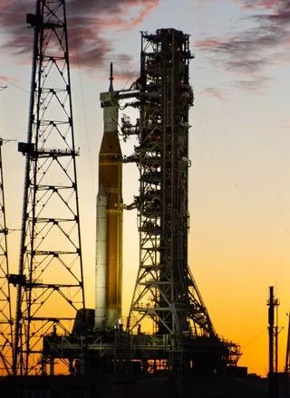 A tall crop showing the rocket and its launch tower silhouetted against an orange sky